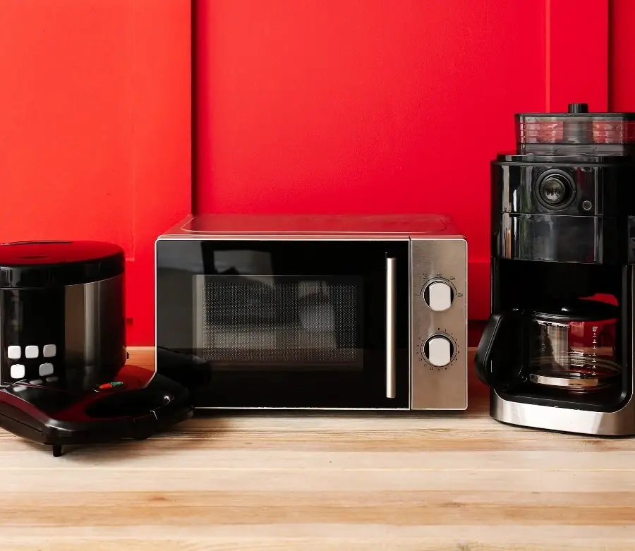 A waffle maker, toaster oven, and coffee maker in front of a bright red wall.