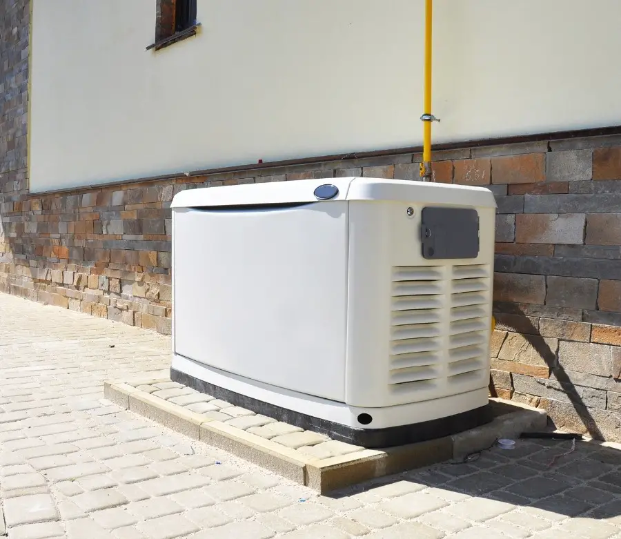 A white stationary generator sitting on a low platform outside of a home.